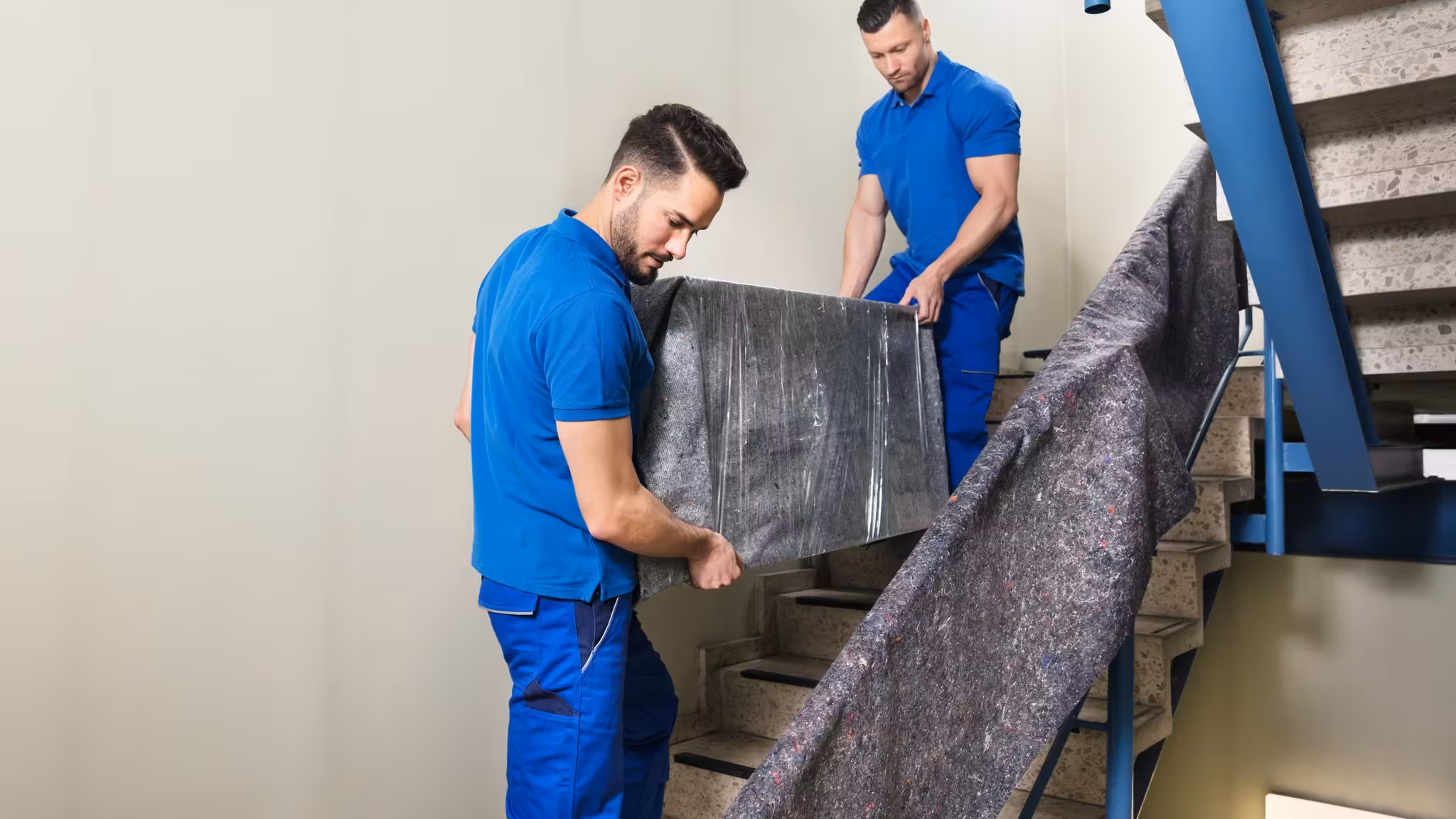 Two movers carrying a rolled carpet up a staircase