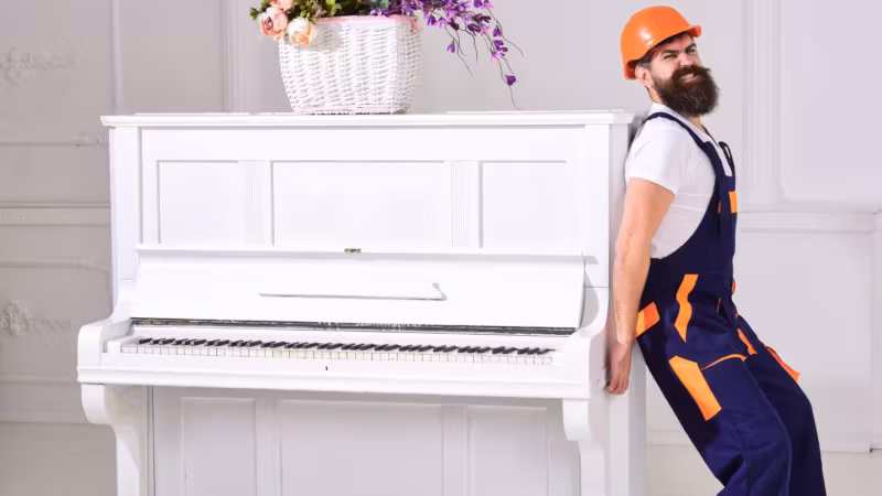 A mover braced against an upright piano