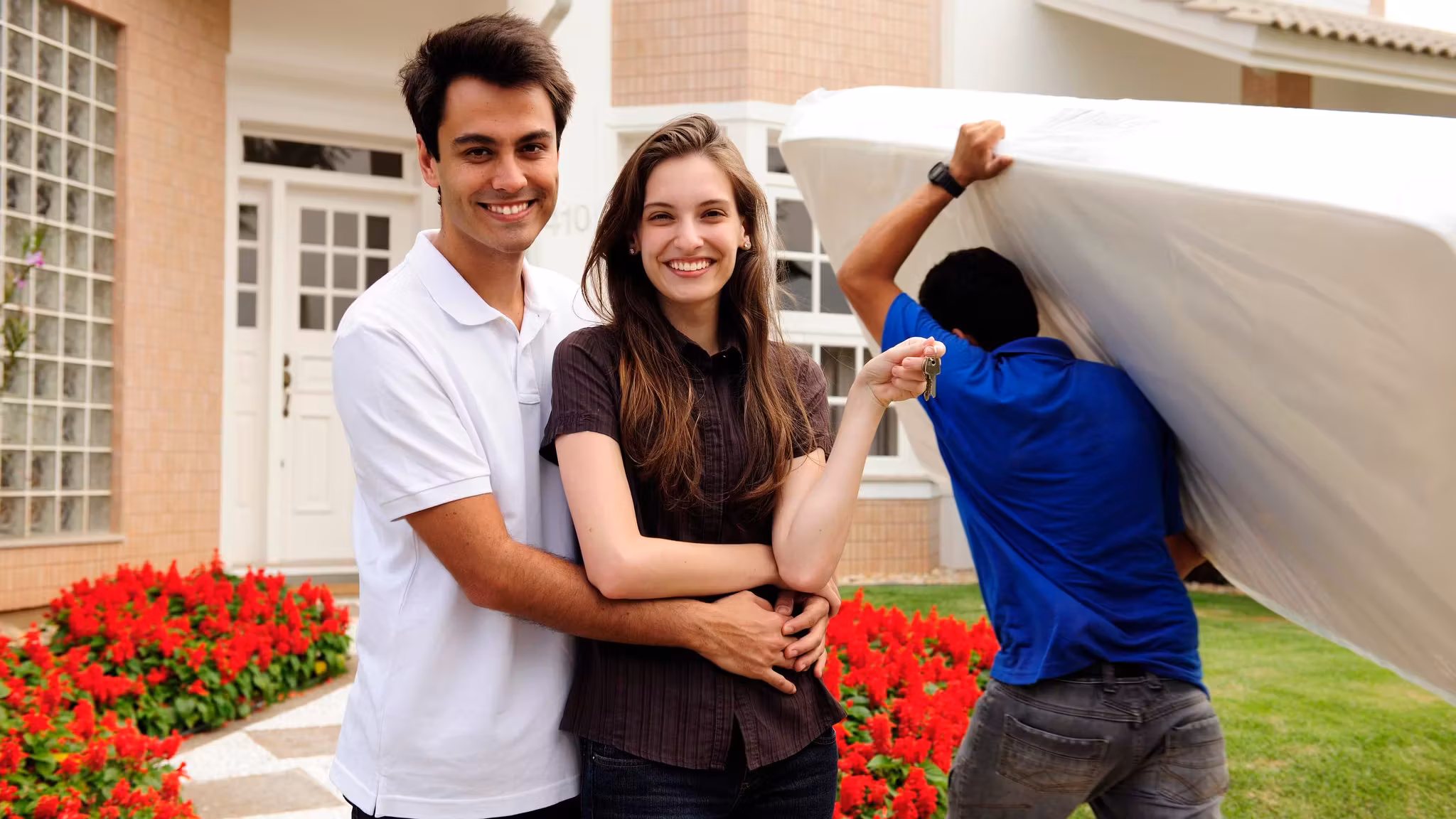 A couple standing outside their house while a mover works at the curb behind them