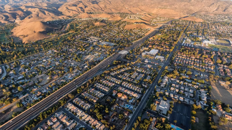Aerial view of a California town spread along a freeway below dry hills