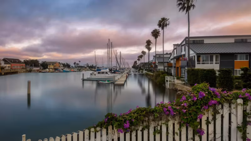 Boats moored beside waterfront houses in California behind a white picket fence