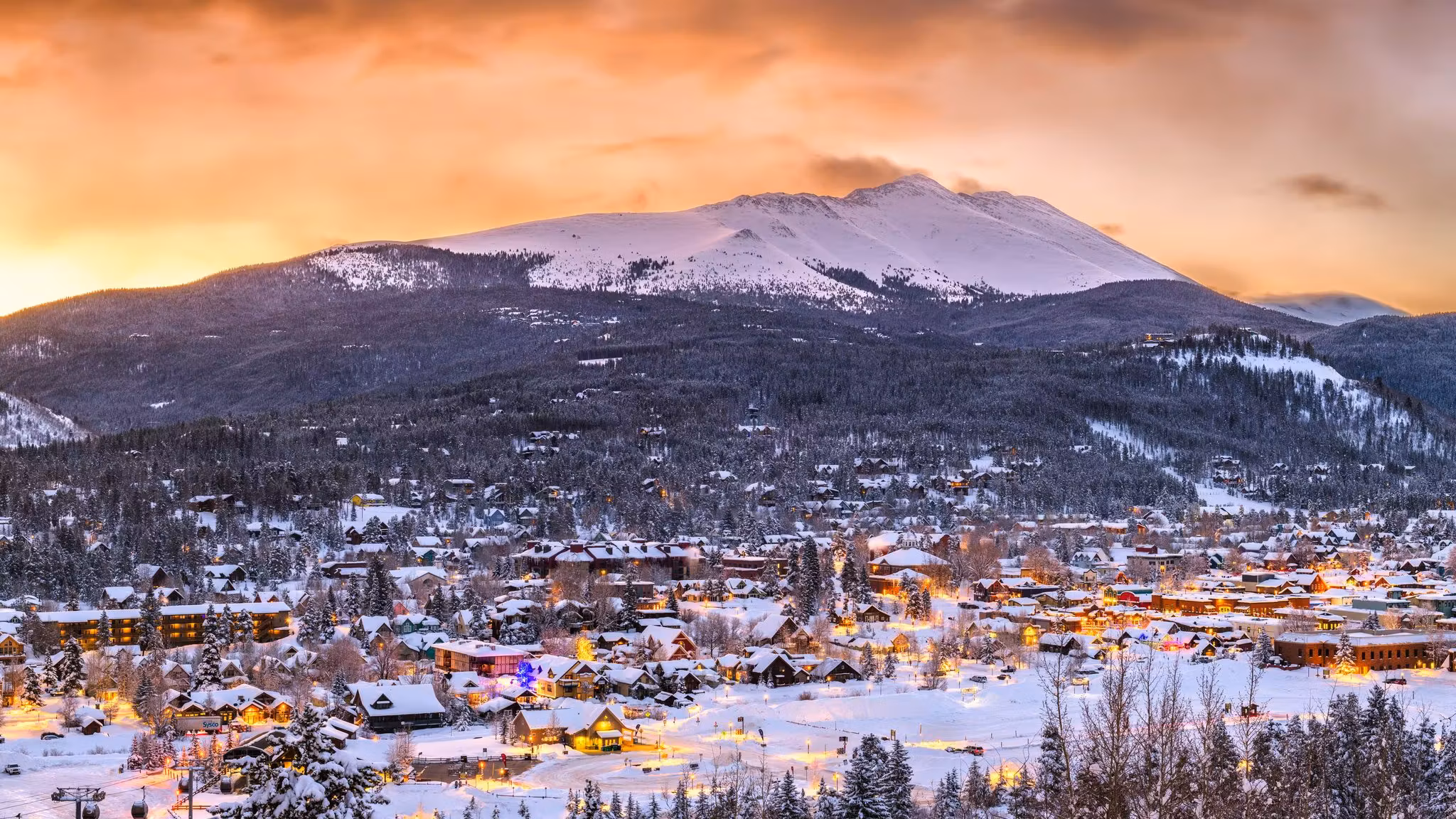 A Colorado mountain town lit at dusk below a snow-covered peak