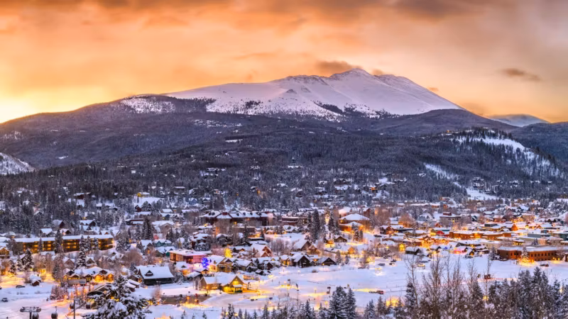 A Colorado mountain town lit at dusk below a snow-covered peak
