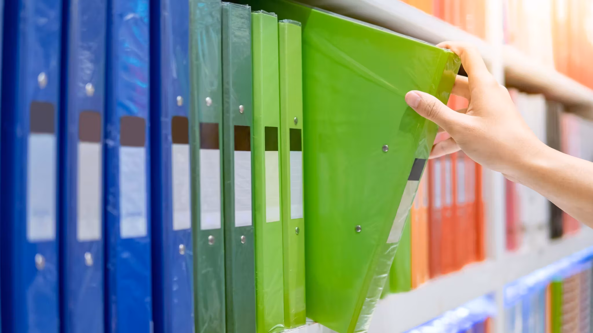 A hand drawing one file from a shelf of colored lever-arch binders