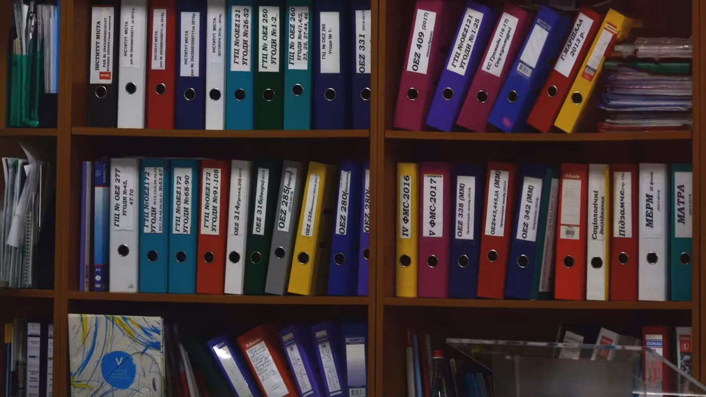 A wall of archive binders on shelves, each spine labeled