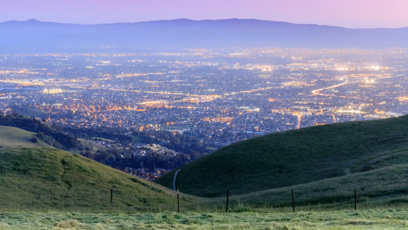 Lights of the East Bay spread out below green hills at dusk