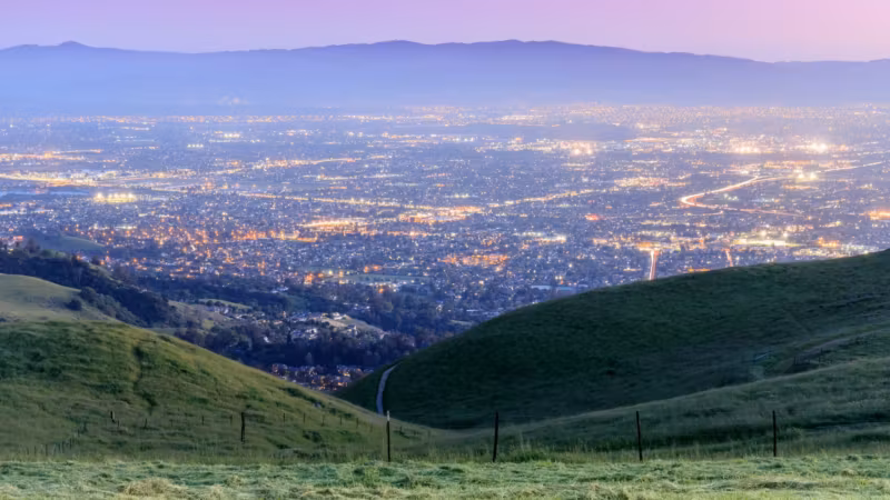Lights of the East Bay spread out below green hills at dusk