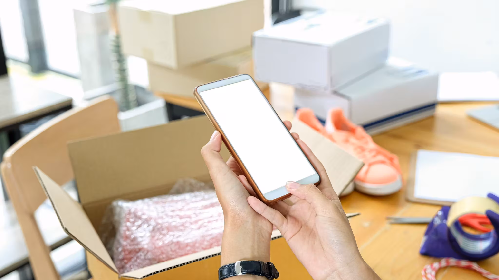 A hand holding a phone above packing materials on a table