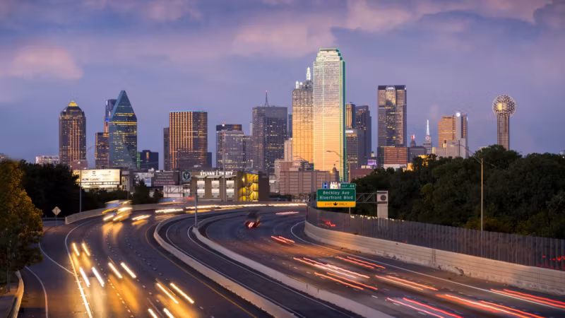 Traffic light trails on a Dallas freeway at dusk with the skyline beyond