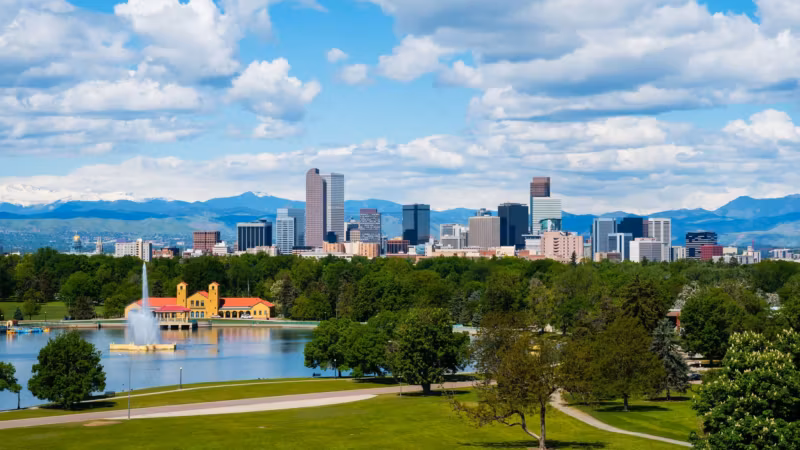 Denver's skyline behind the City Park lake and pavilion, with the Rocky Mountains on the horizon