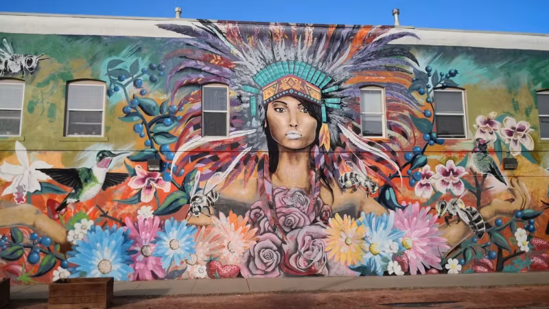 A large mural of a woman in a feathered headdress painted on the side of a Denver building