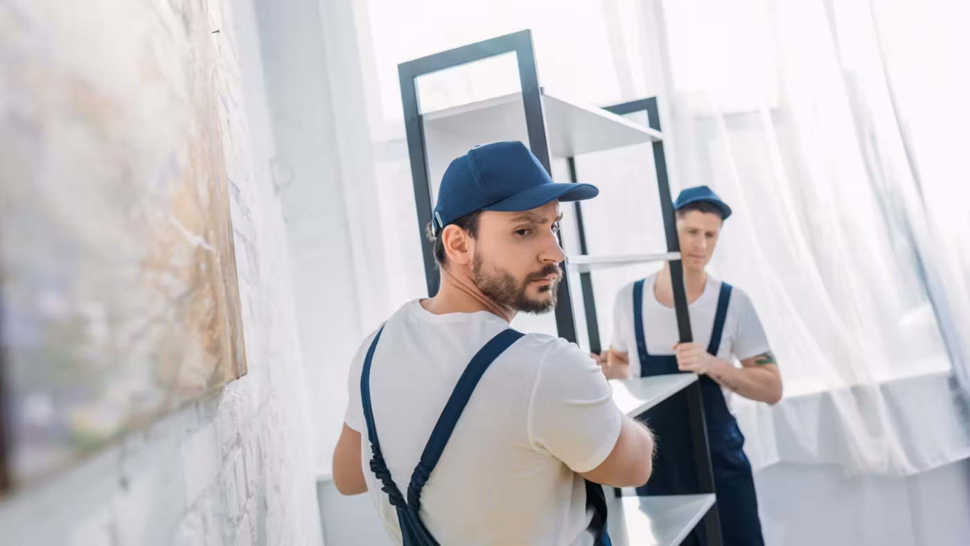 Two movers steadying a tall framed mirror beside a window
