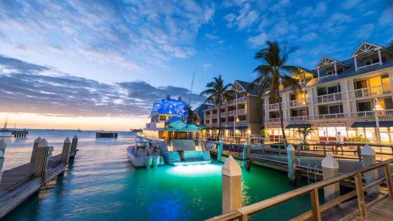 A marina in Florida at dusk with a lit boat moored beside waterfront buildings