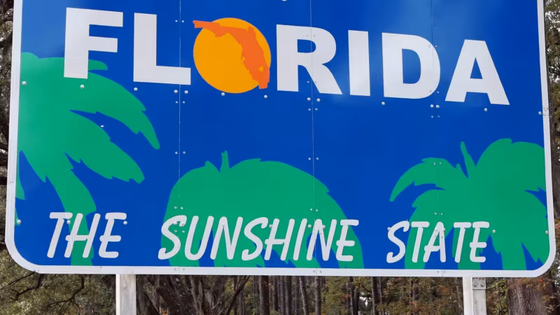 A Welcome to Florida sign among pines beside the road