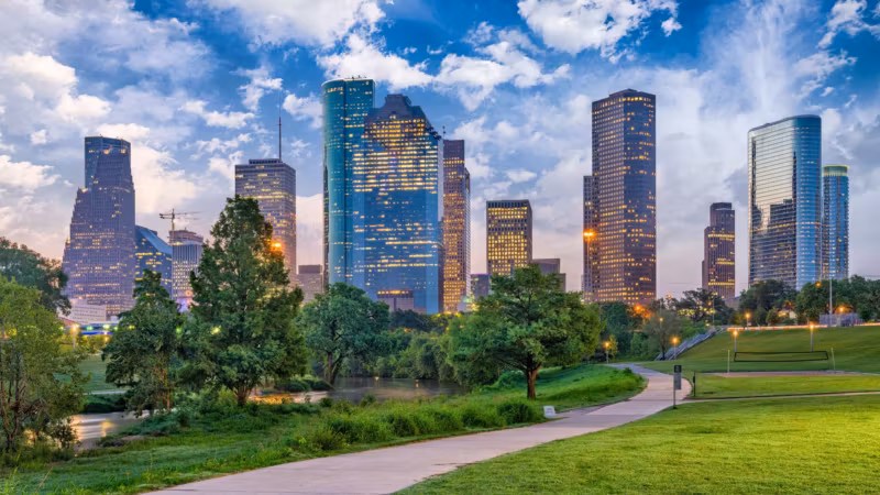 A park path curving toward the lit Houston skyline at dusk