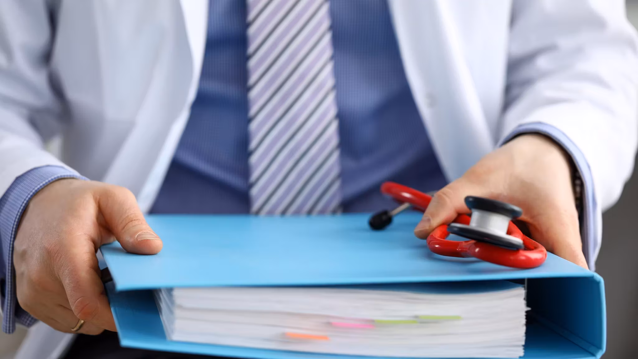 A hand passing a blue ring binder across a desk