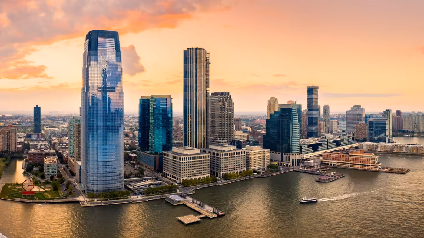 The Jersey City waterfront at sunset, its glass towers standing on the Hudson