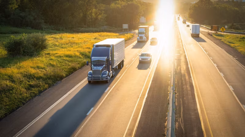 Trucks on a divided highway at sunrise, the sun low on the road ahead