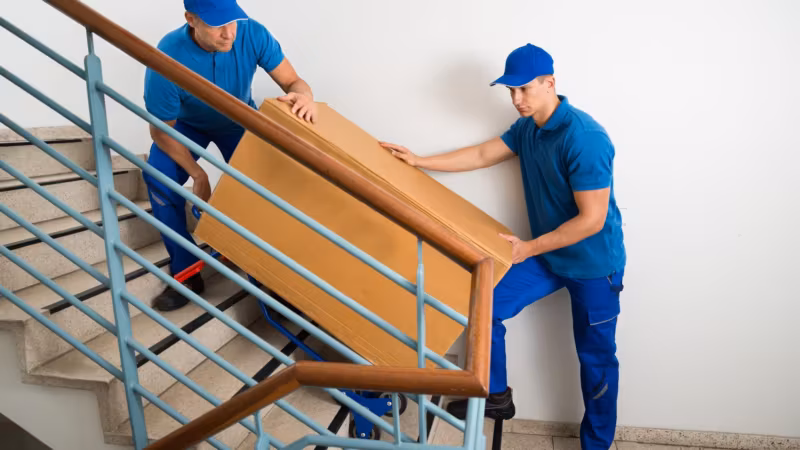 Two movers carrying a wooden table down an external staircase