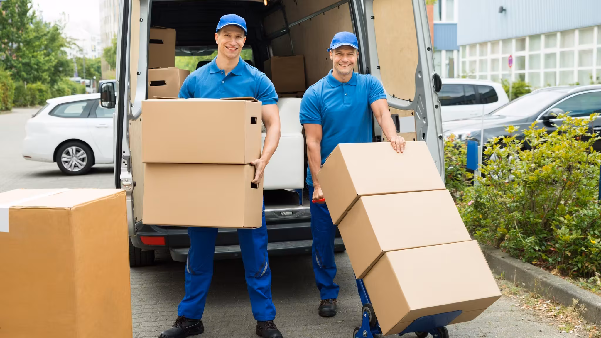 Two movers behind an open van with a hand truck stacked with cartons