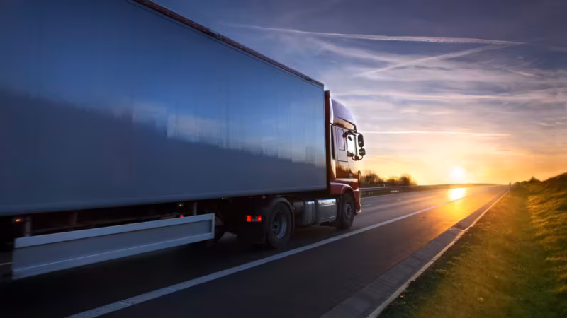 A tractor-trailer traveling a highway at sunset