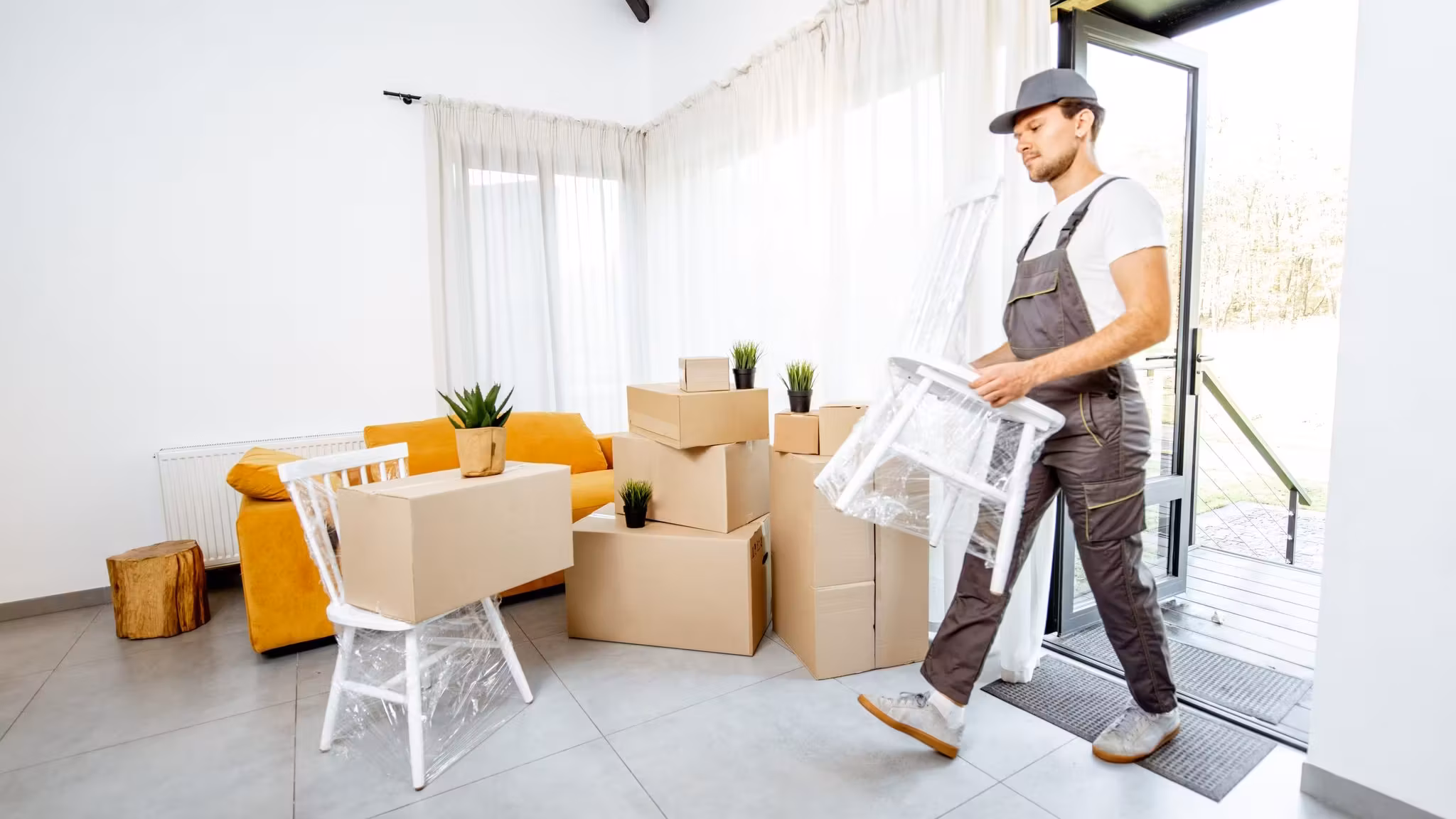 A mover carrying a wrapped chair out through an open door into daylight
