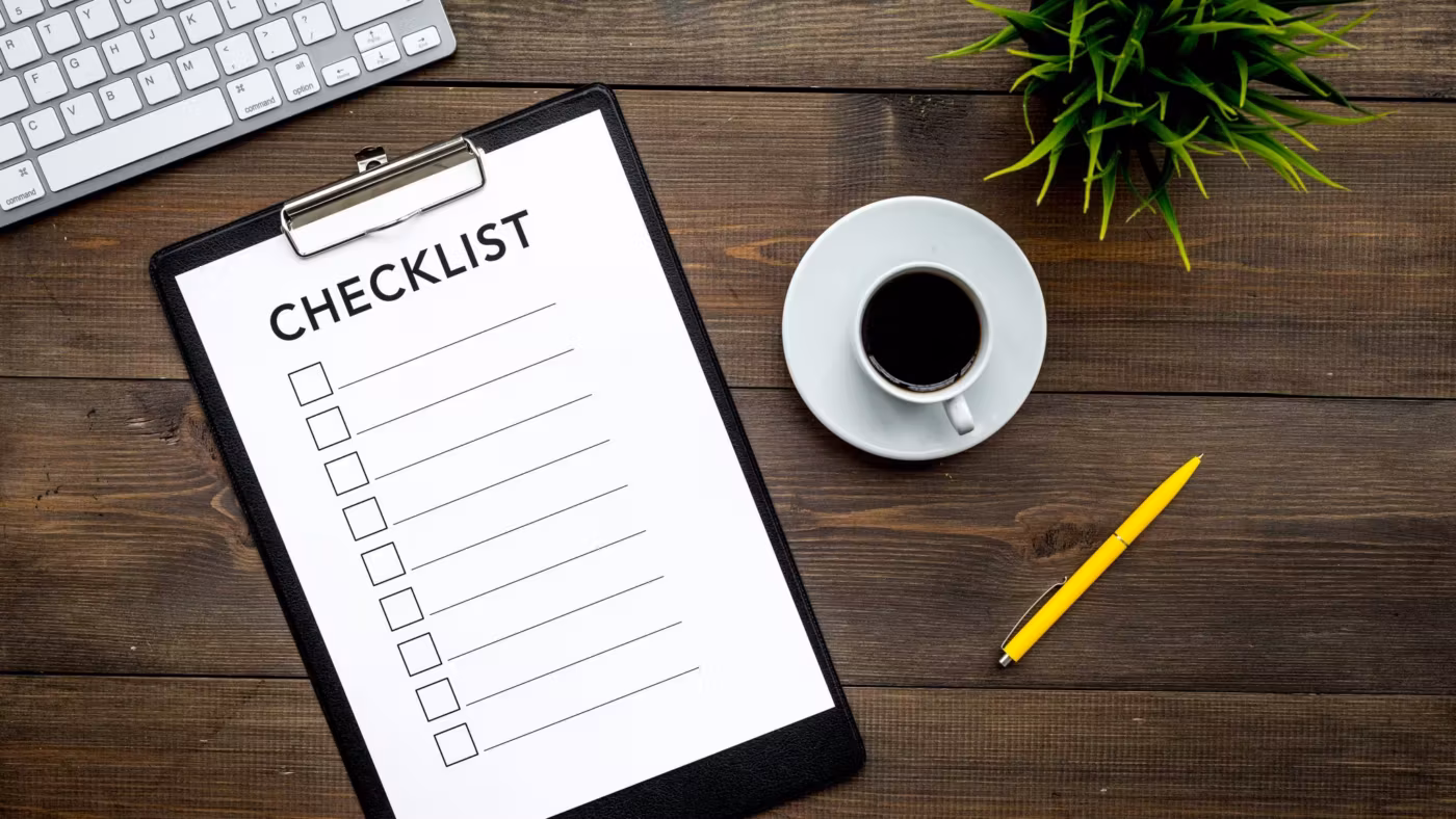 A printed checklist on a clipboard beside a keyboard, a pencil and a cup of coffee