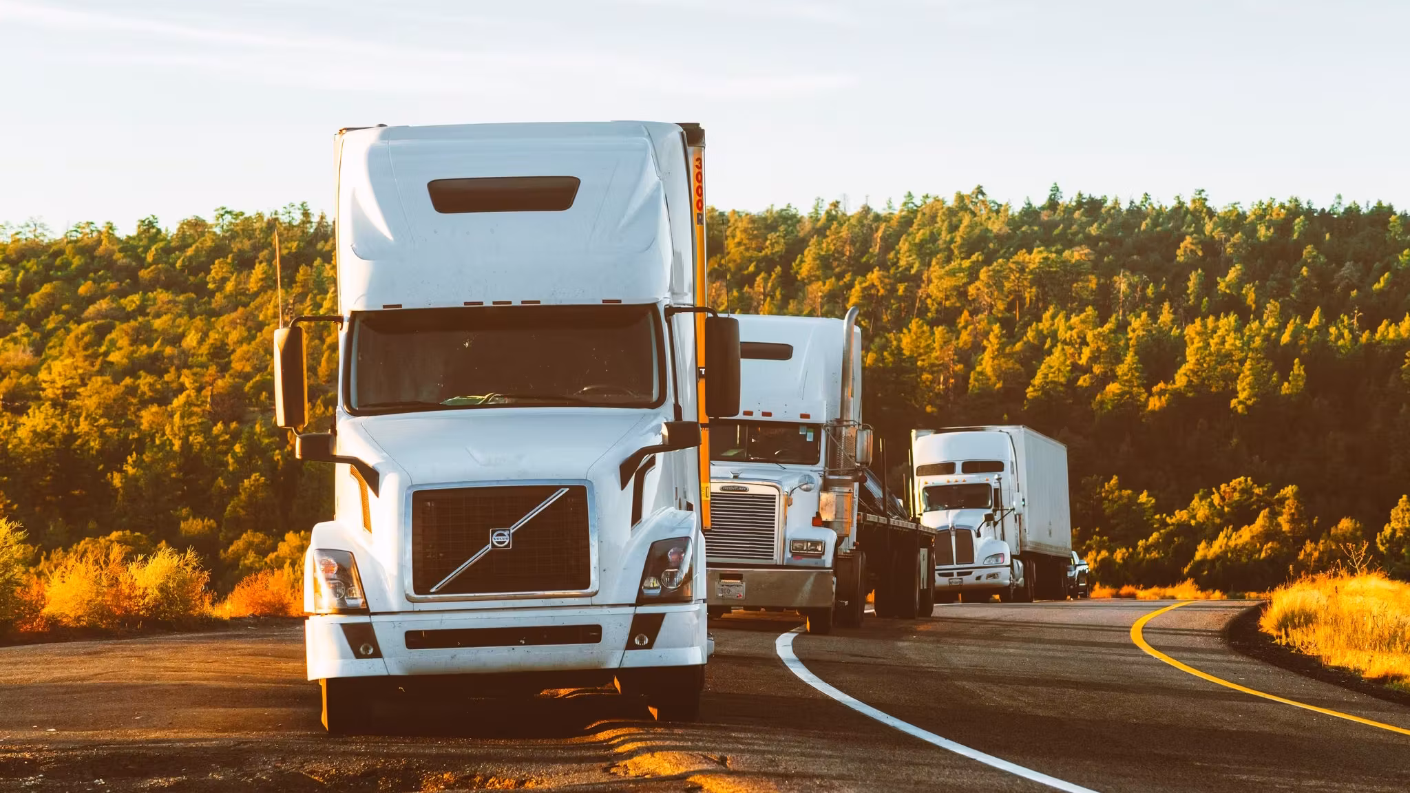 Three trucks on a highway curve through open high country at golden hour