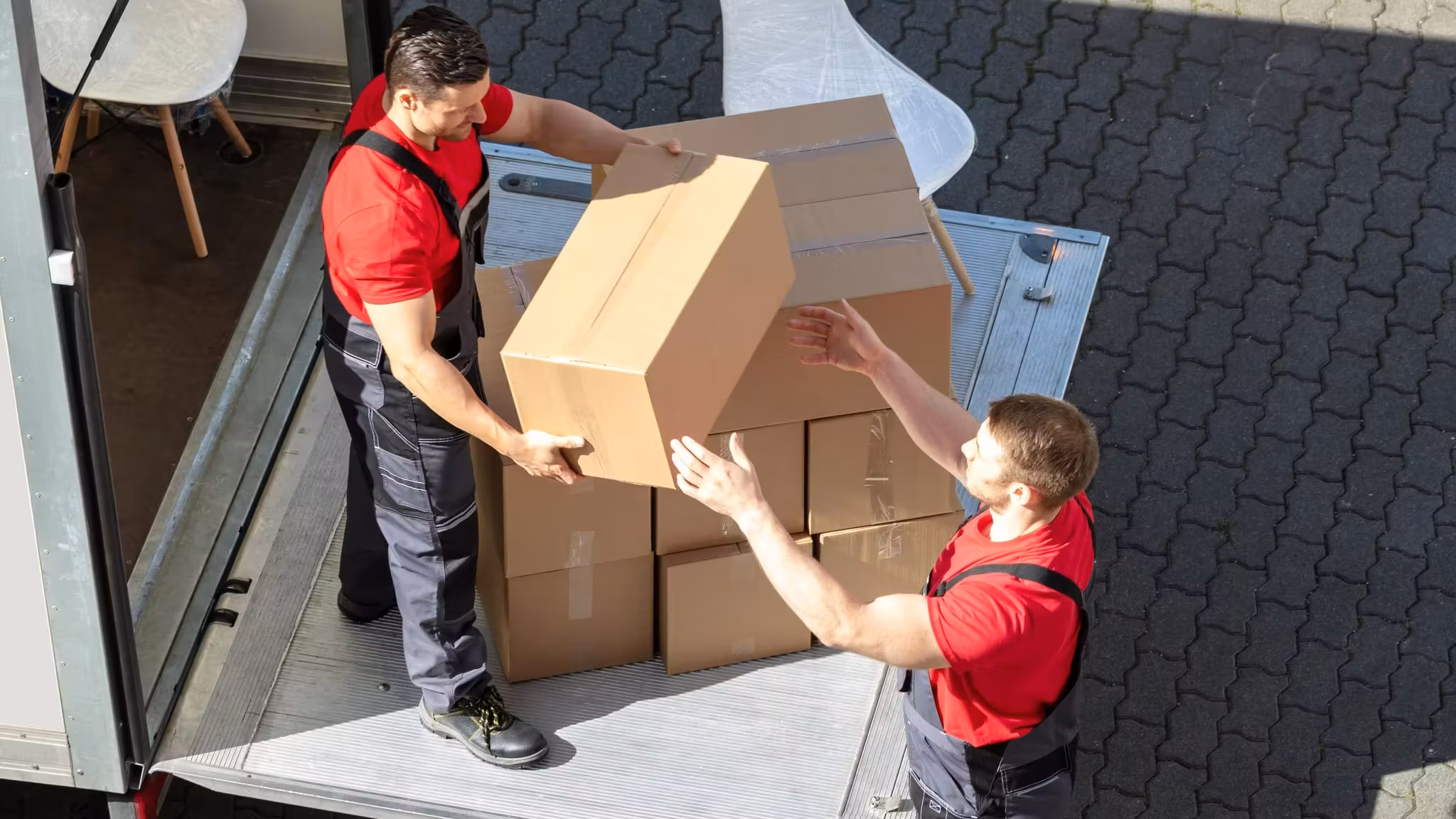 Two movers passing a carton between them at the tail lift of a truck