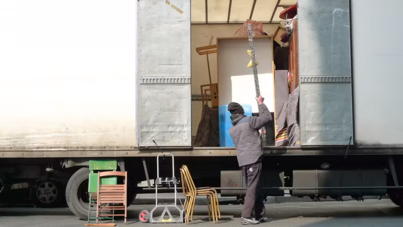 A mover loading stacked chairs into a trailer with its side curtain open