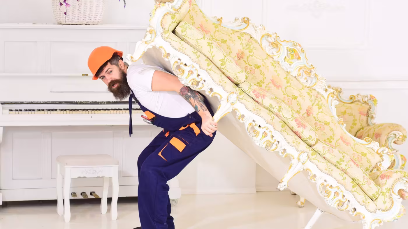 A mover carrying an ornate sofa through a pale room