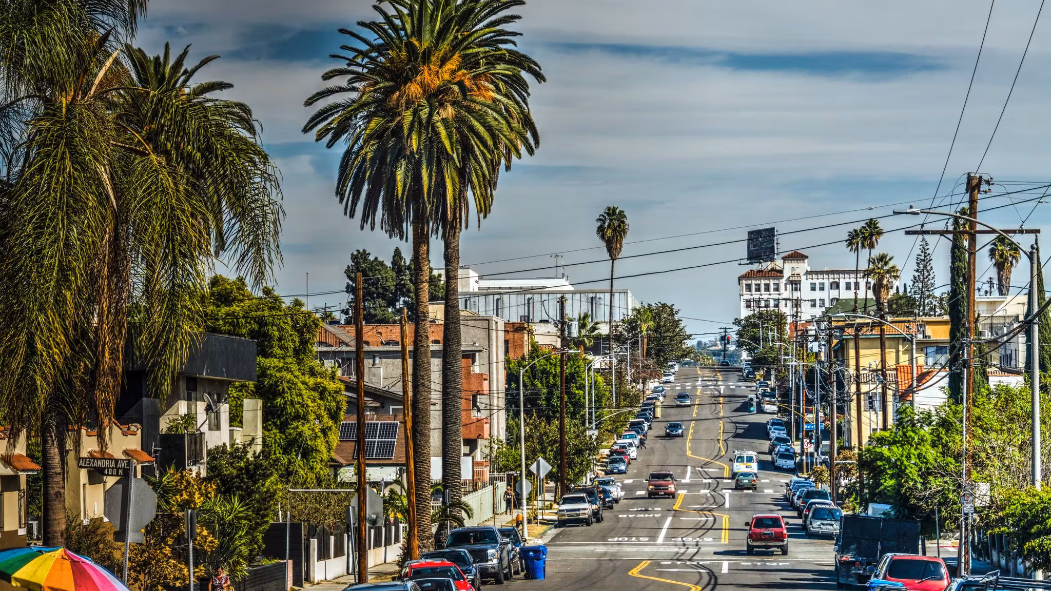 A Los Angeles street sloping downhill between palms and parked cars