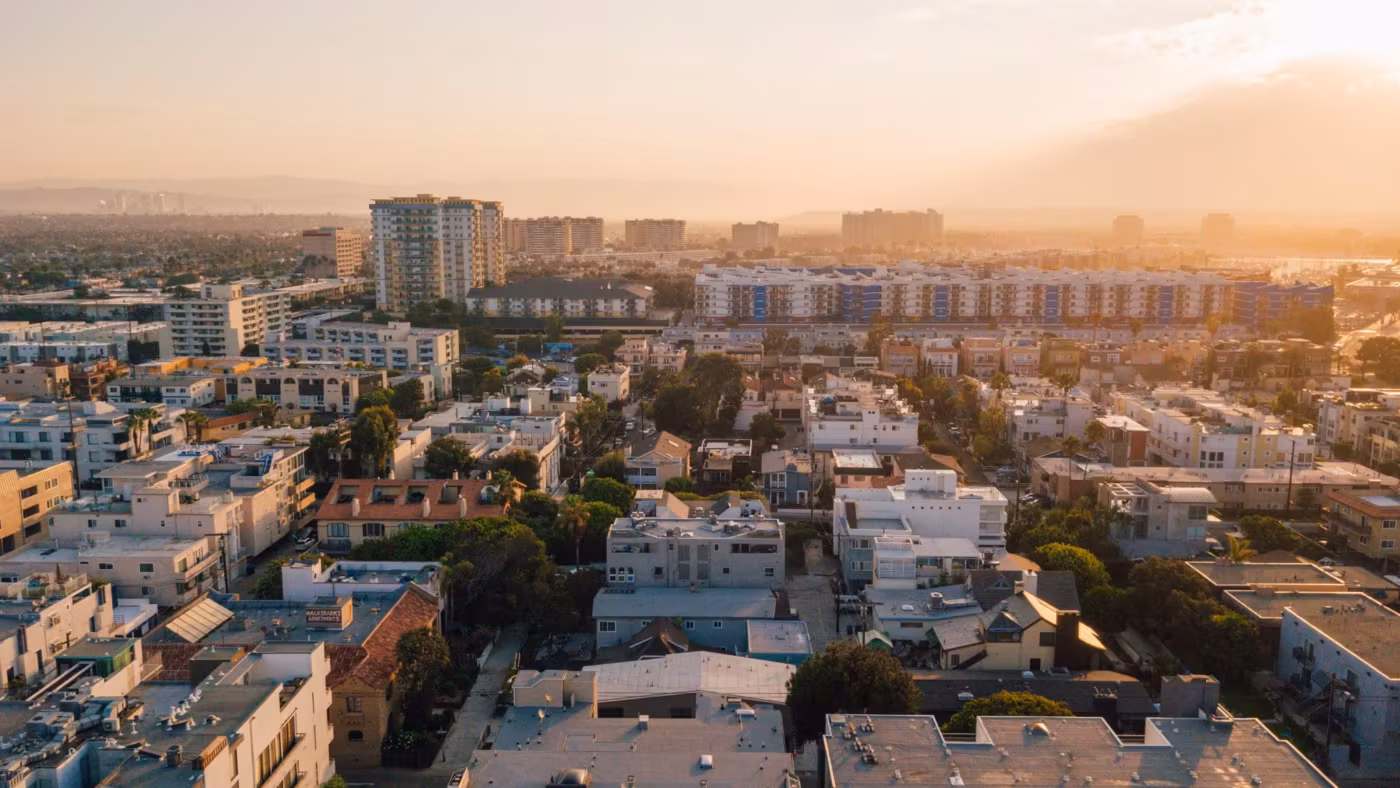 Los Angeles rooftops and low apartment blocks reaching toward the coast at sunset