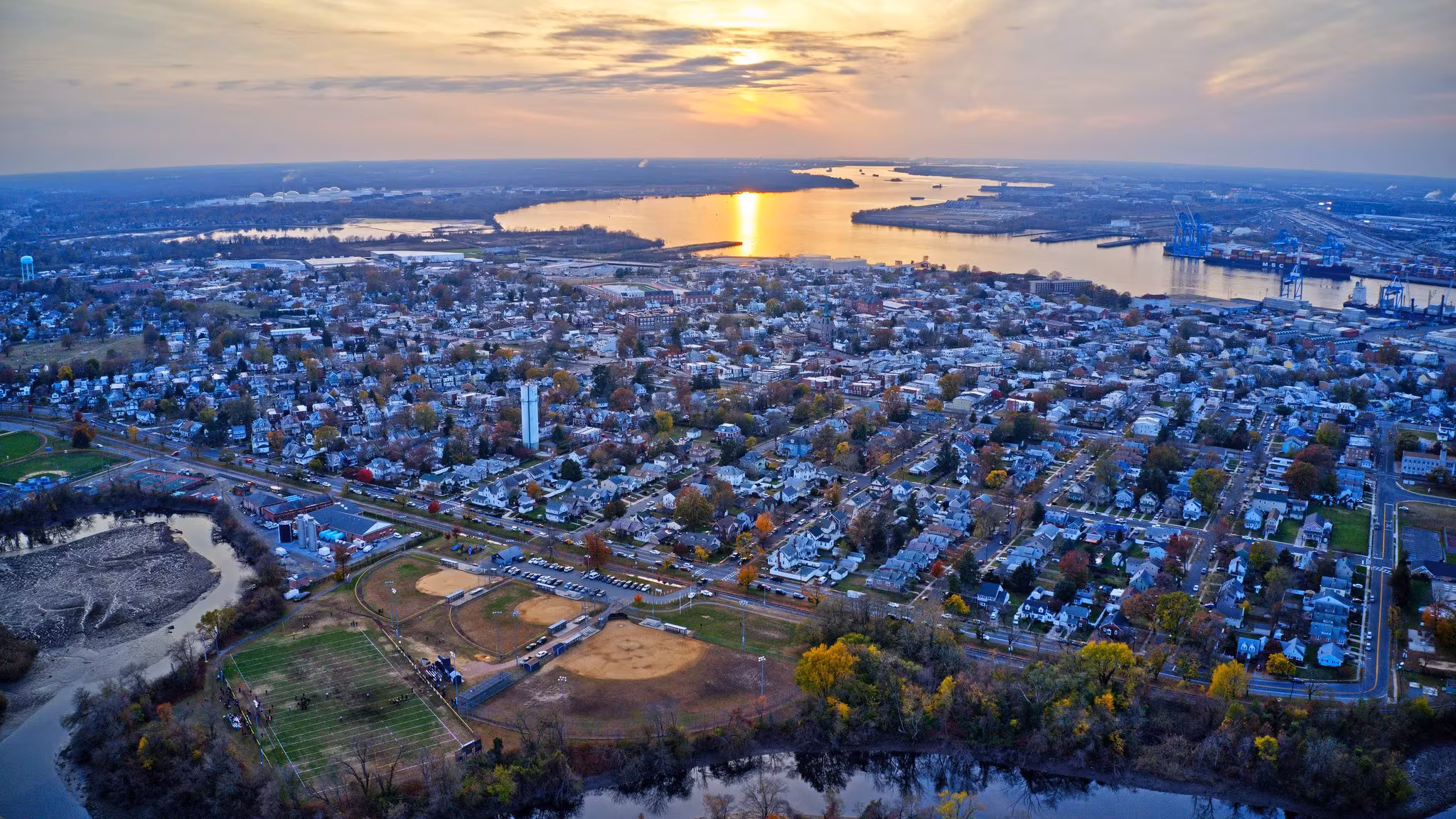 Aerial view over a New Jersey town at sunset, streets of low houses reaching the river