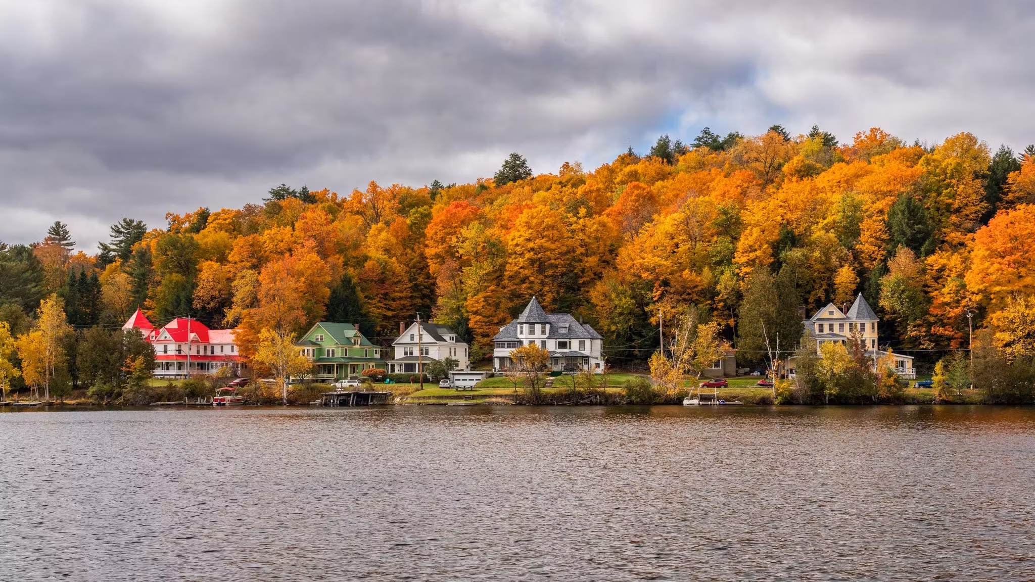Houses along a lakeshore below autumn woods in upstate New York