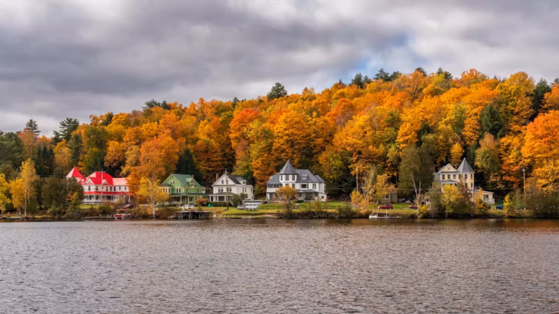Houses along a lakeshore below autumn woods in upstate New York