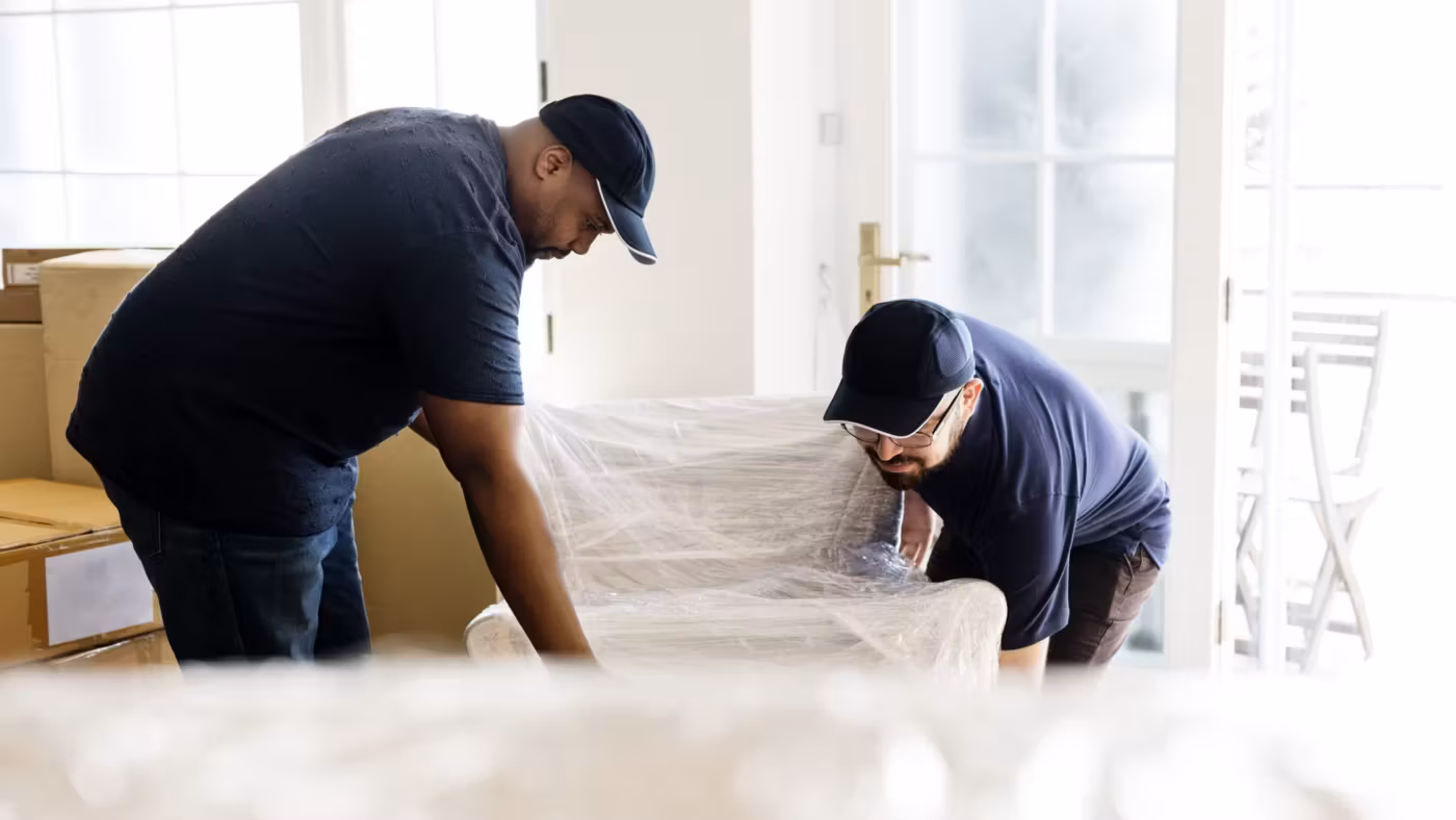 A mover bent over a large wrapped item, checking its cover