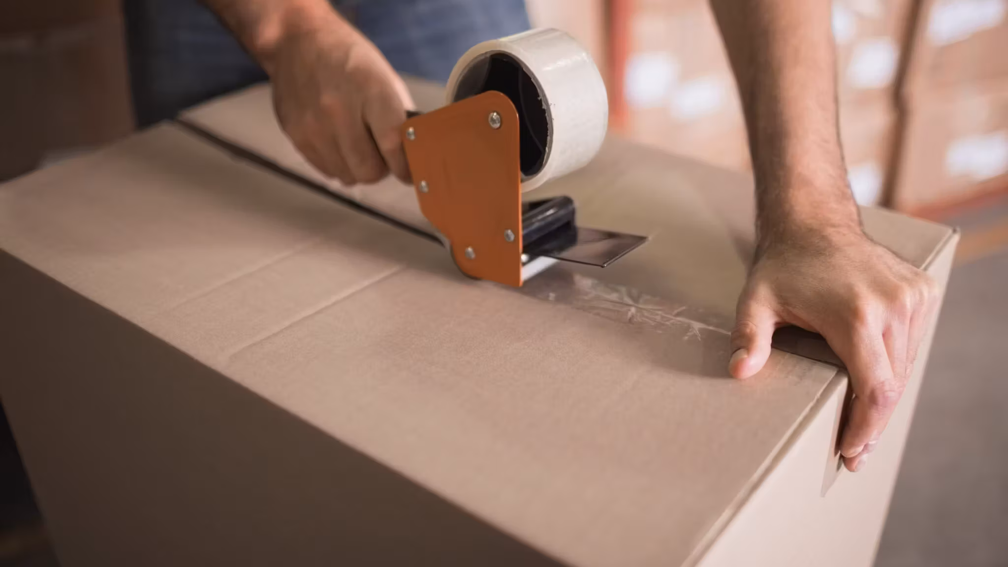 A mover's hands running a tape gun along the seam of a large carton