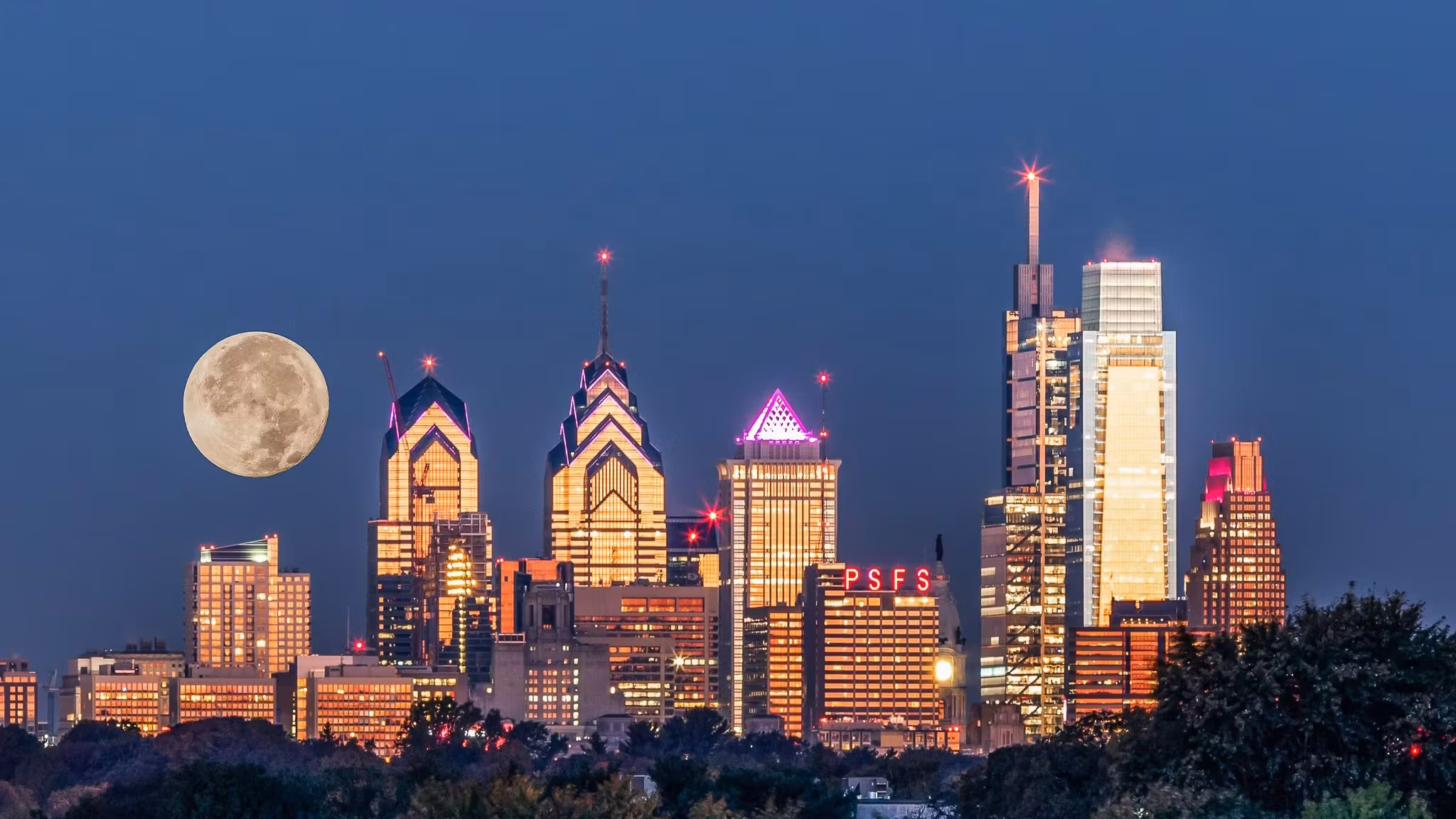 A full moon rising beside the Philadelphia skyline at dusk
