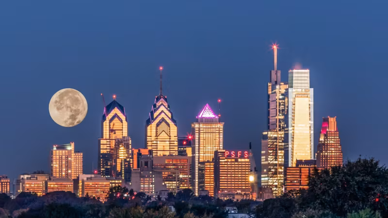 A full moon rising beside the Philadelphia skyline at dusk
