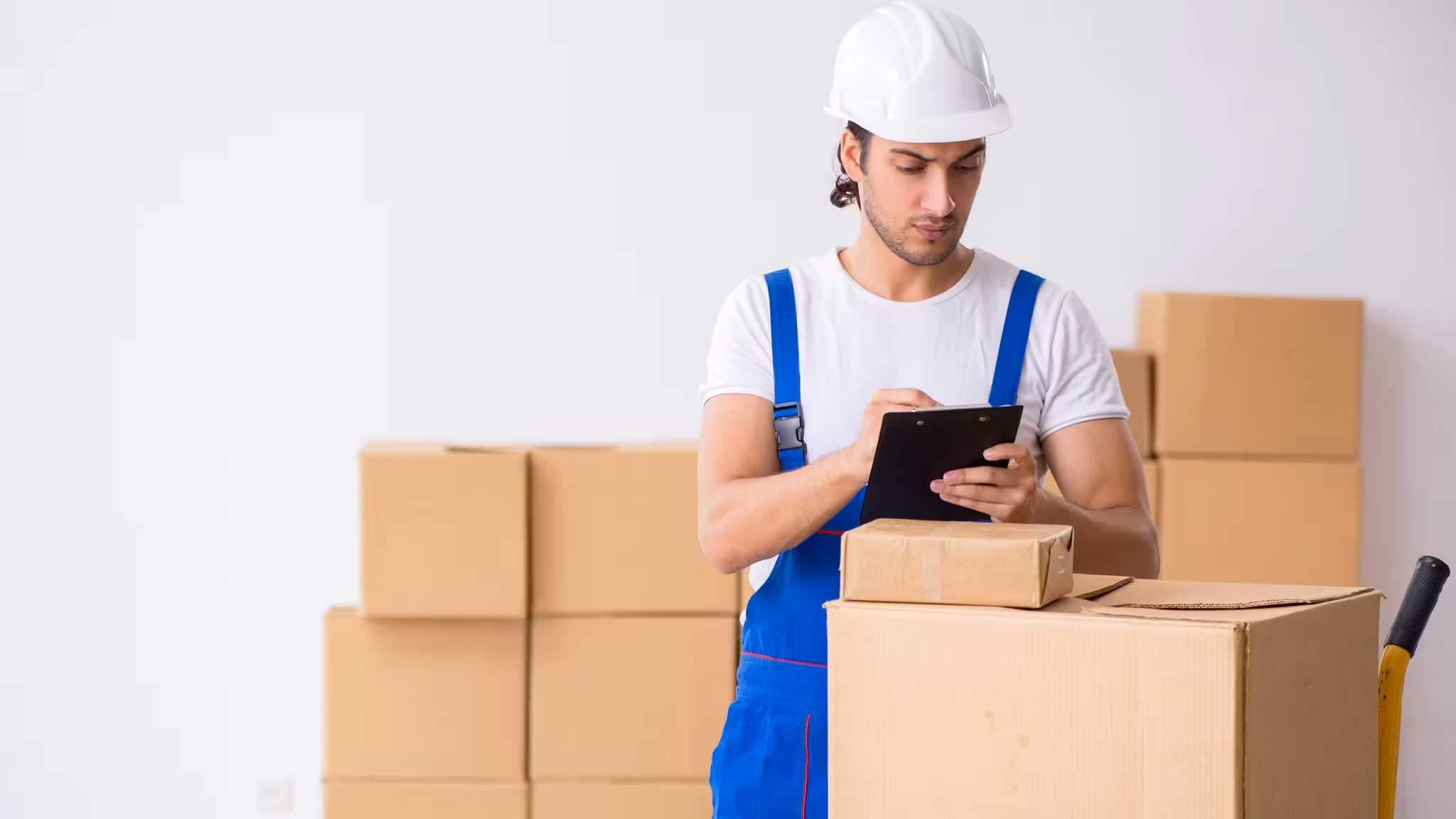 A mover reading from a tablet beside a wall of stacked cartons