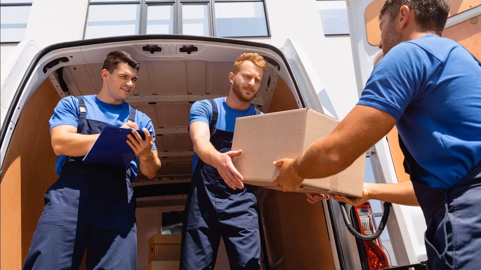 Two movers loading a van from a hand truck at the curb