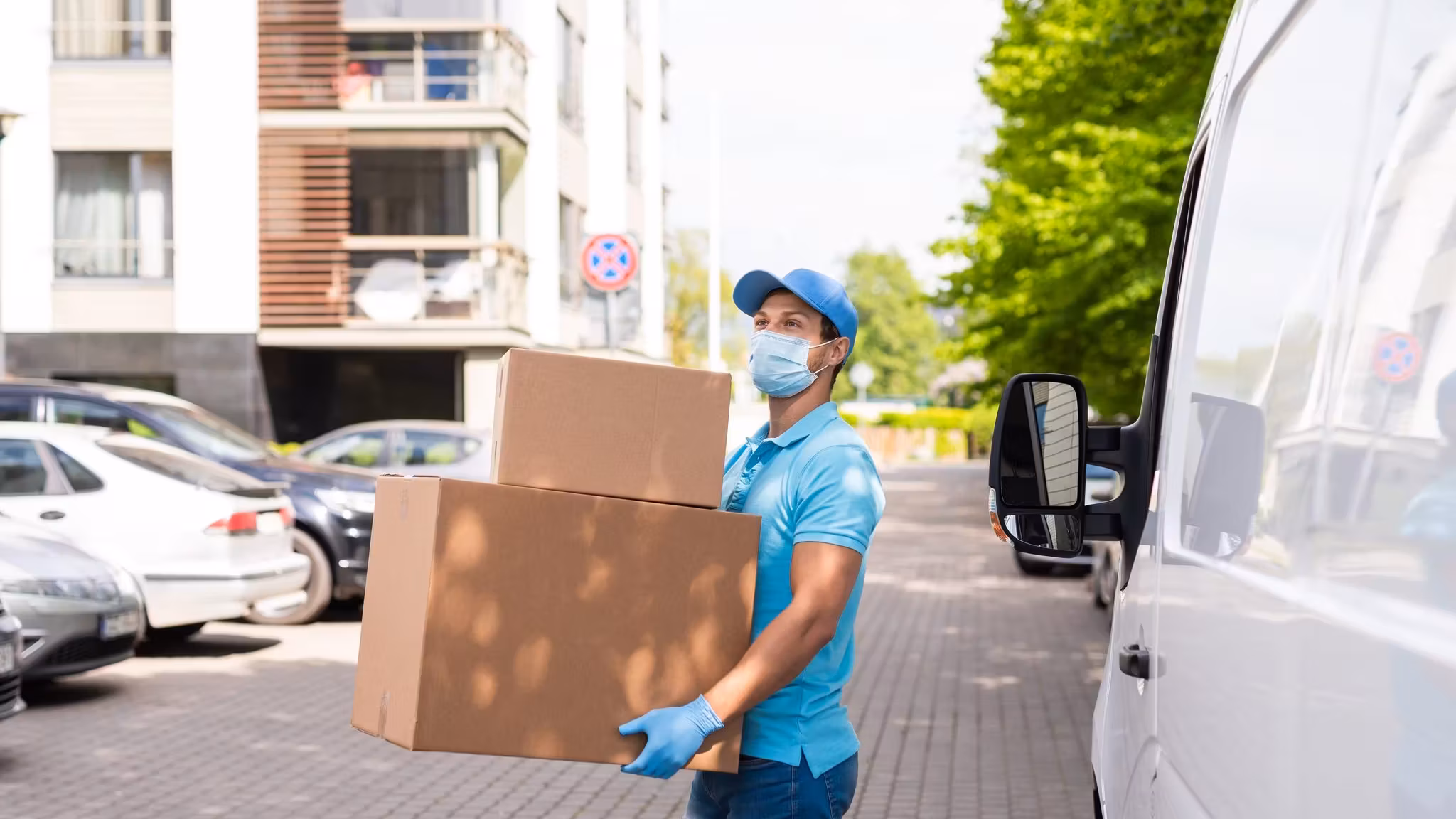 A mover carrying a carton beside a van on a tree-lined street