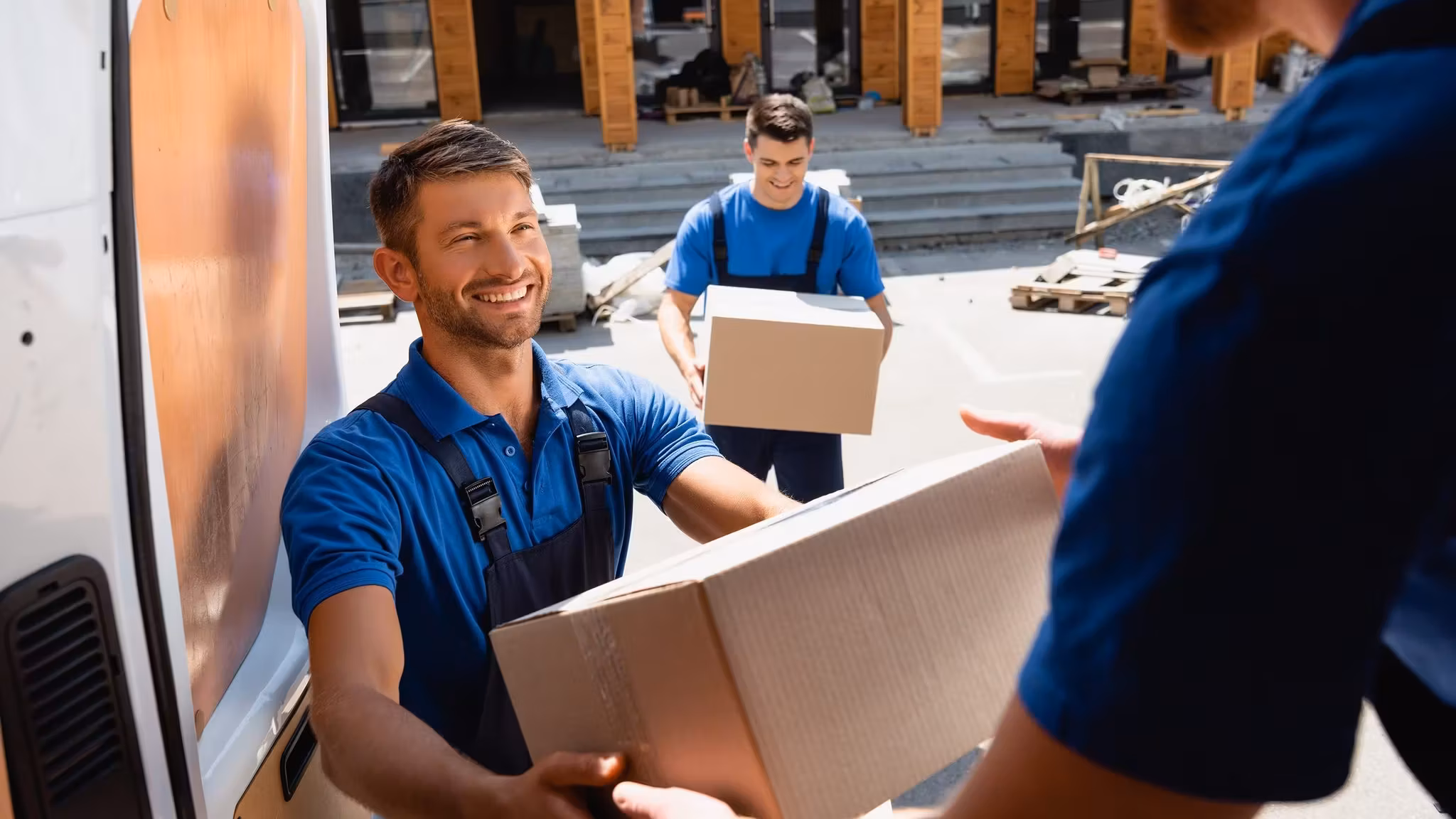Two movers handing a carton between them at the side of a van