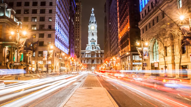 Broad Street in Philadelphia at night, traffic drawn out in light trails toward City Hall