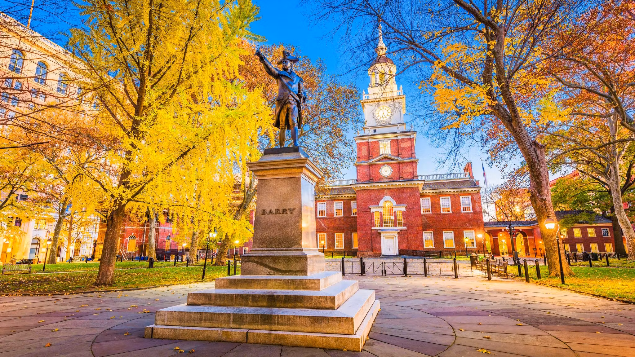 Independence Hall in Philadelphia behind a statue and autumn trees