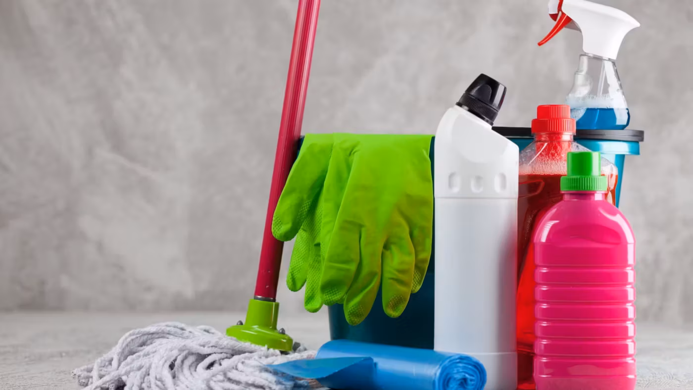Household chemical bottles and a spray grouped on a floor beside a mop and rubber gloves