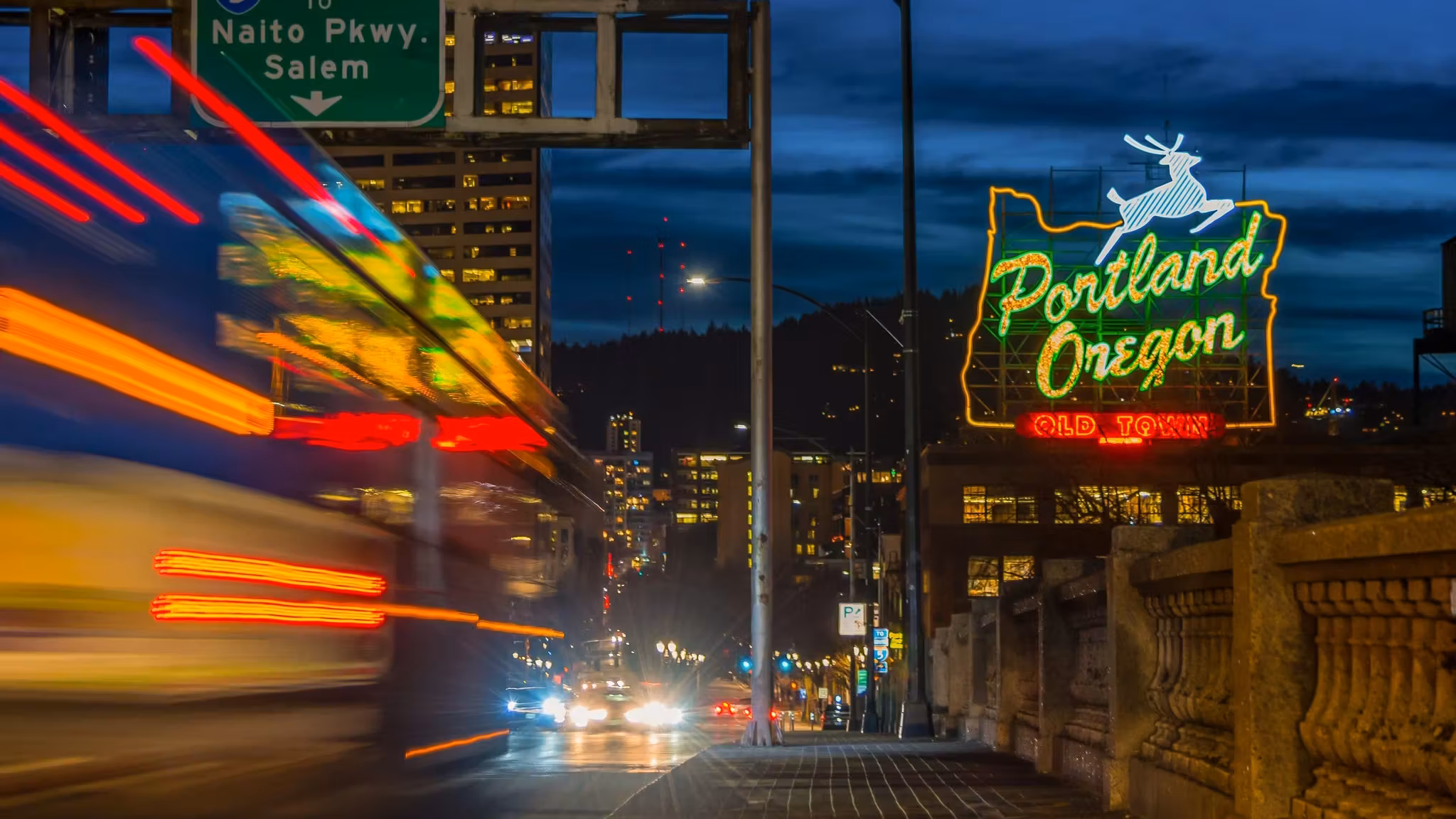 The Portland Oregon neon sign over Old Town with a bus passing in a blur of light