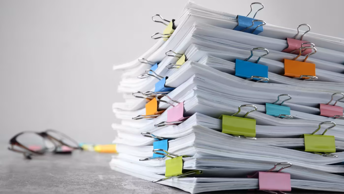 A tall stack of clipped paper documents on a desk