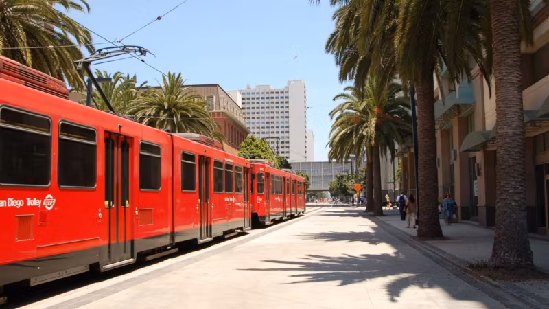 A red San Diego trolley at a palm-lined platform